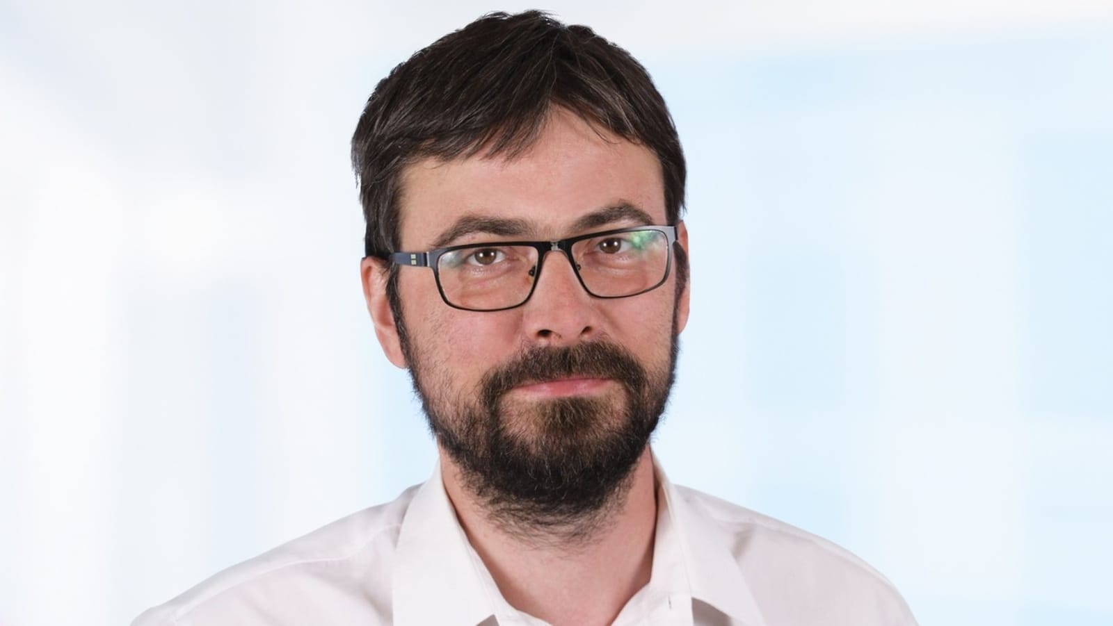 Ondřej Vrbík, a bearded man in glasses and a white shirt, against a light background