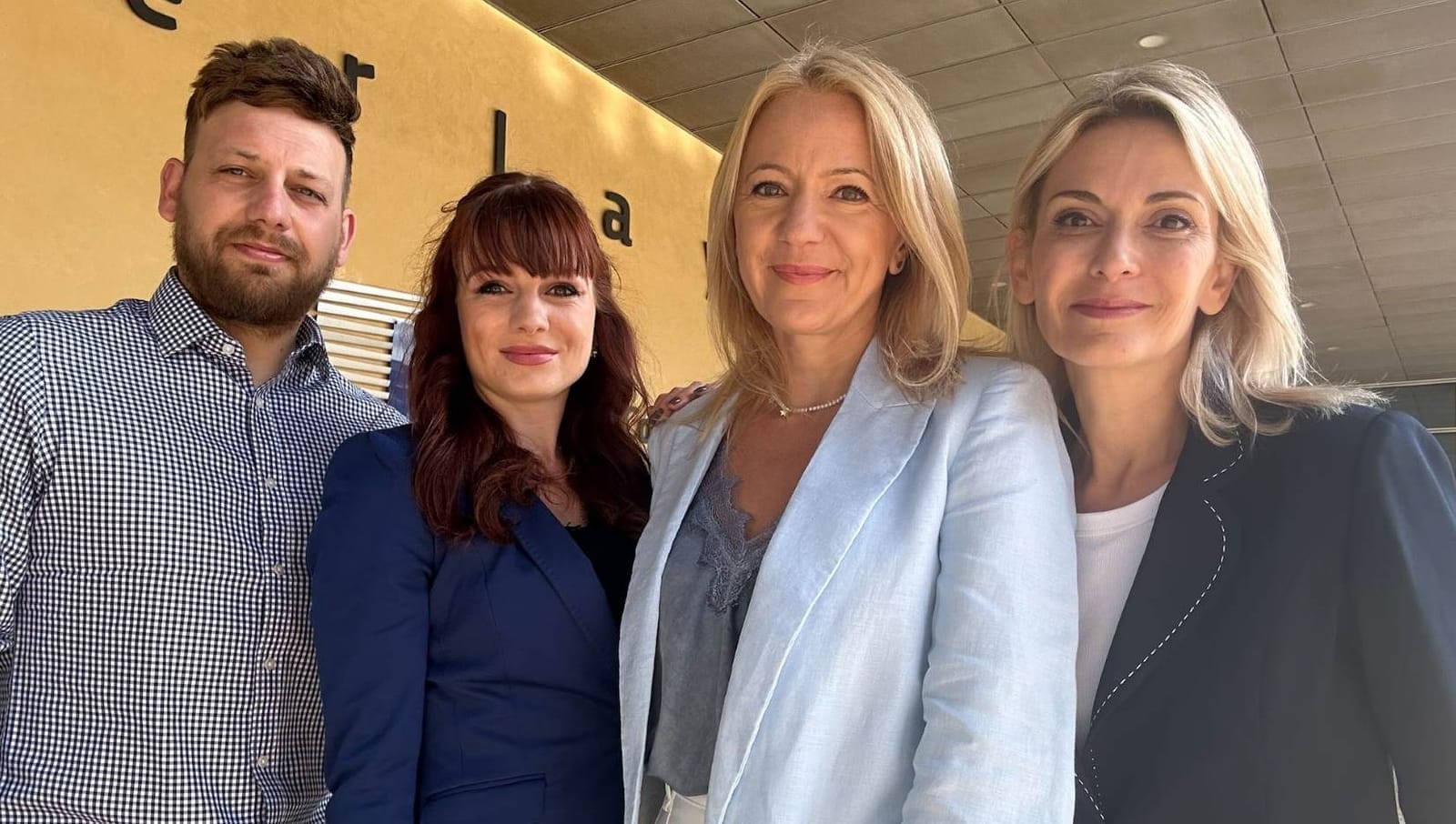 One man and three women of CME's joint Brussels newsroom standing side by side in front of a yellow lettered wall