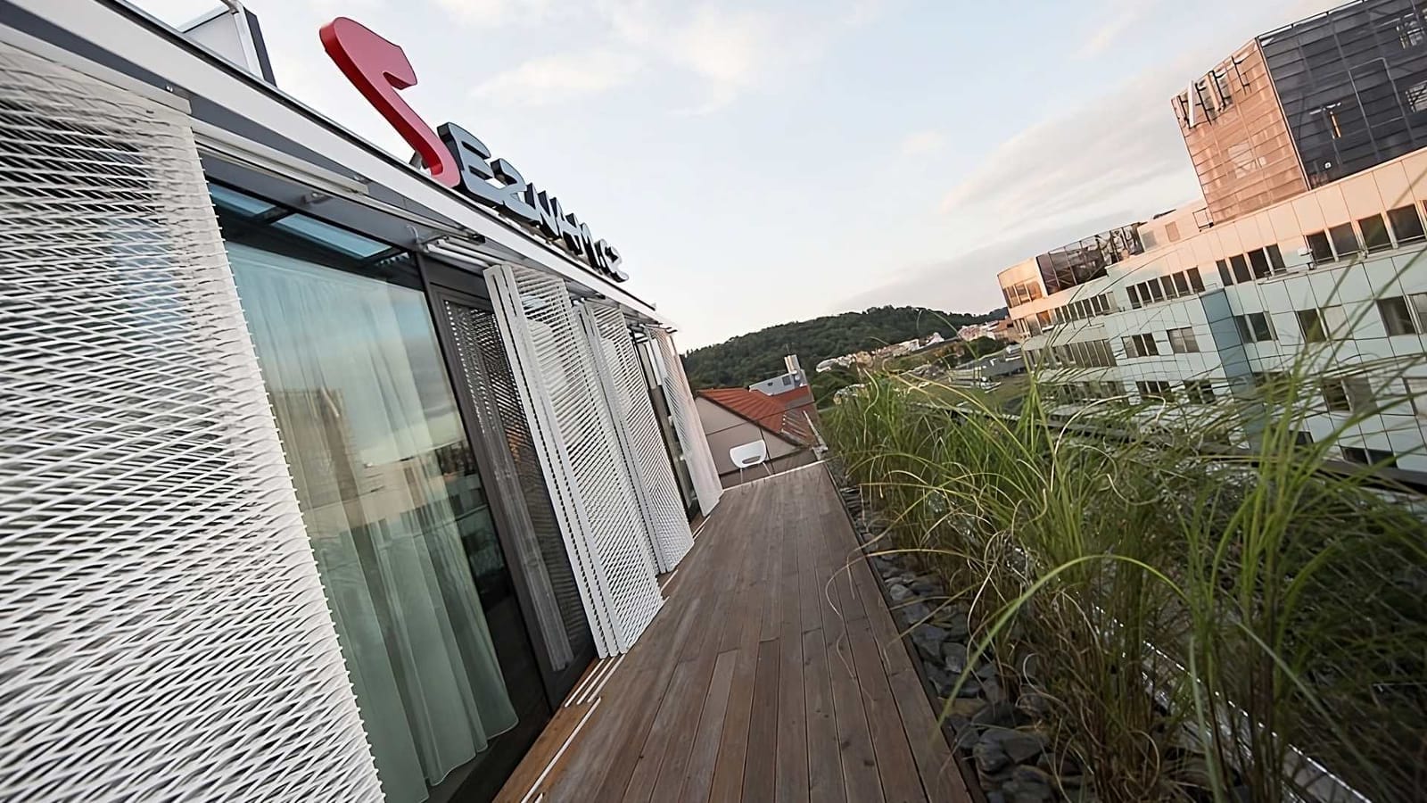 Rooftop terrace with wooden decking and ornamental grasses at the Seznam.cz office complex in Prague's Smíchov district, red company logo above