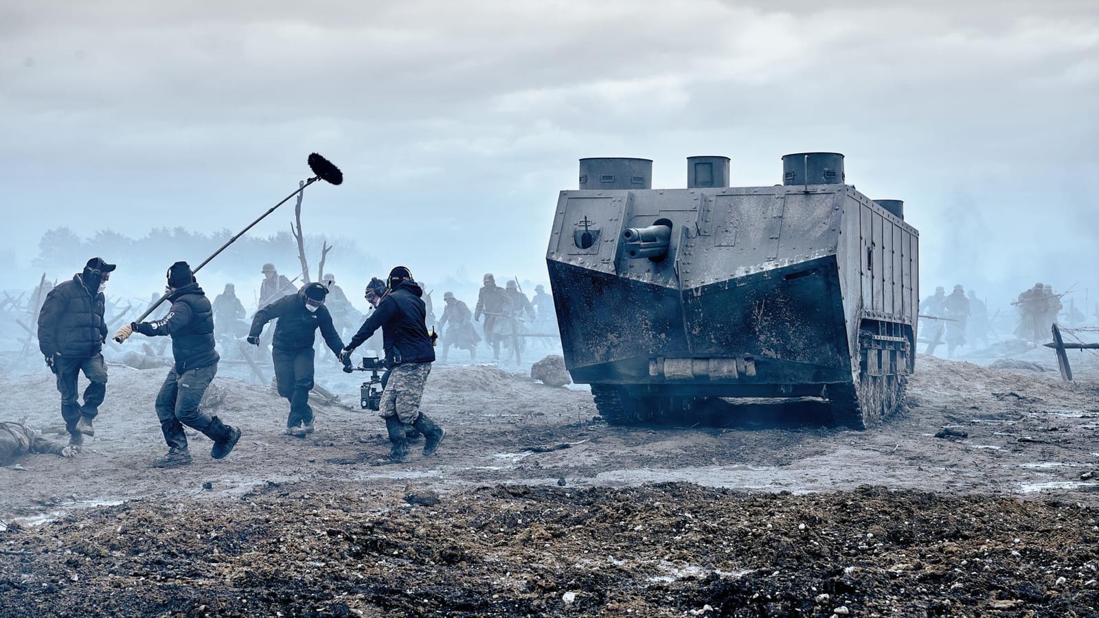 Film crew with boom microphone and camera running alongside a World War I tank on the muddy set of All Quiet on the Western Front for Netflix