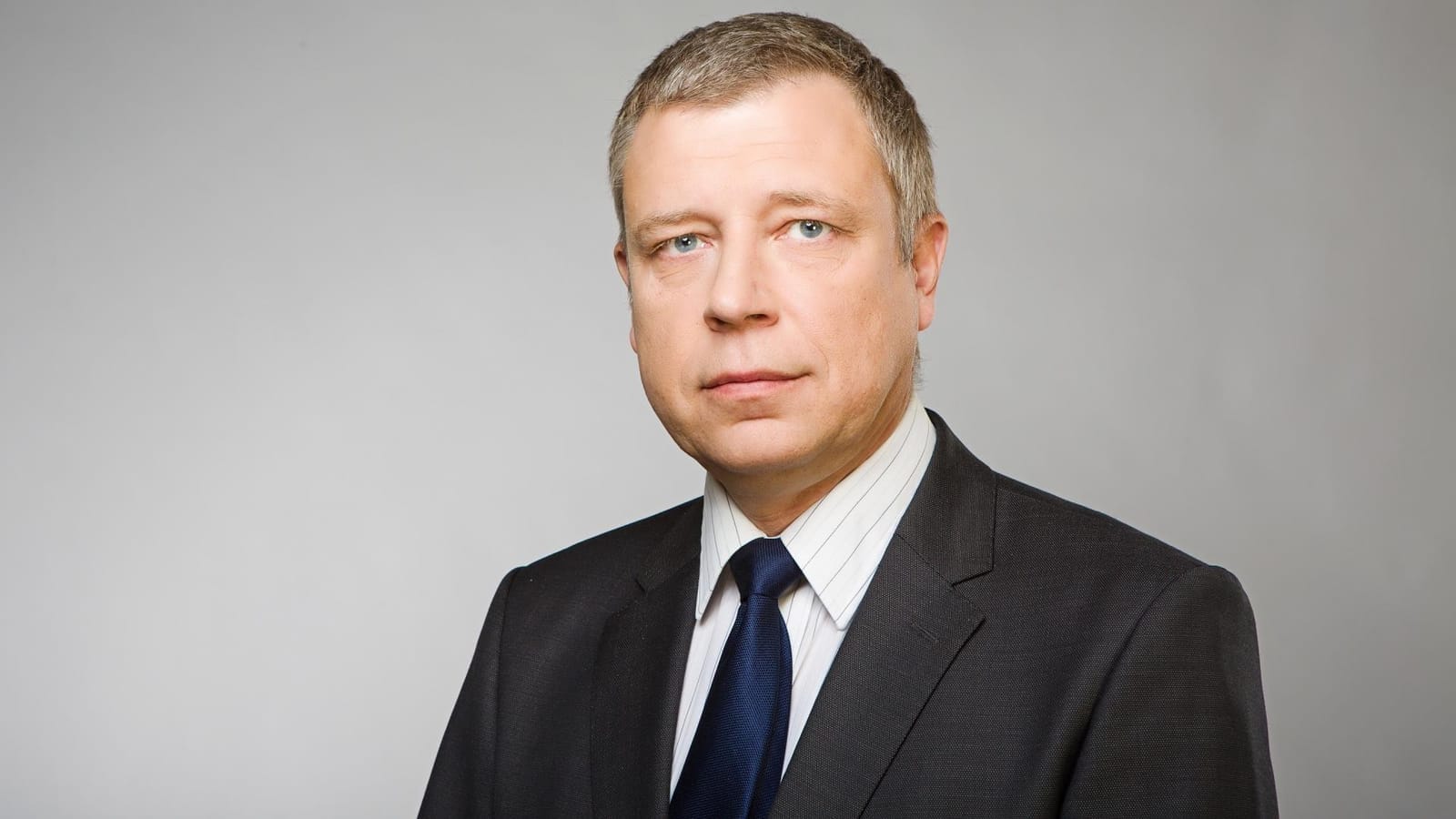 Zdeněk Šámal in a studio portrait, wearing a dark suit, white shirt and dark blue tie against a grey background
