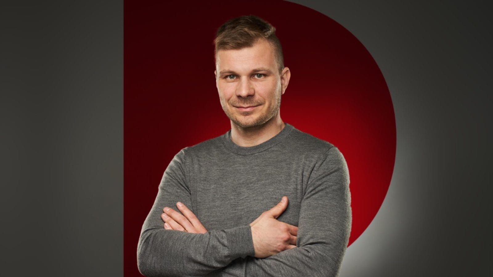 Libor Matoušek in a grey sweater with folded arms, smiling against a dark background with a red circle