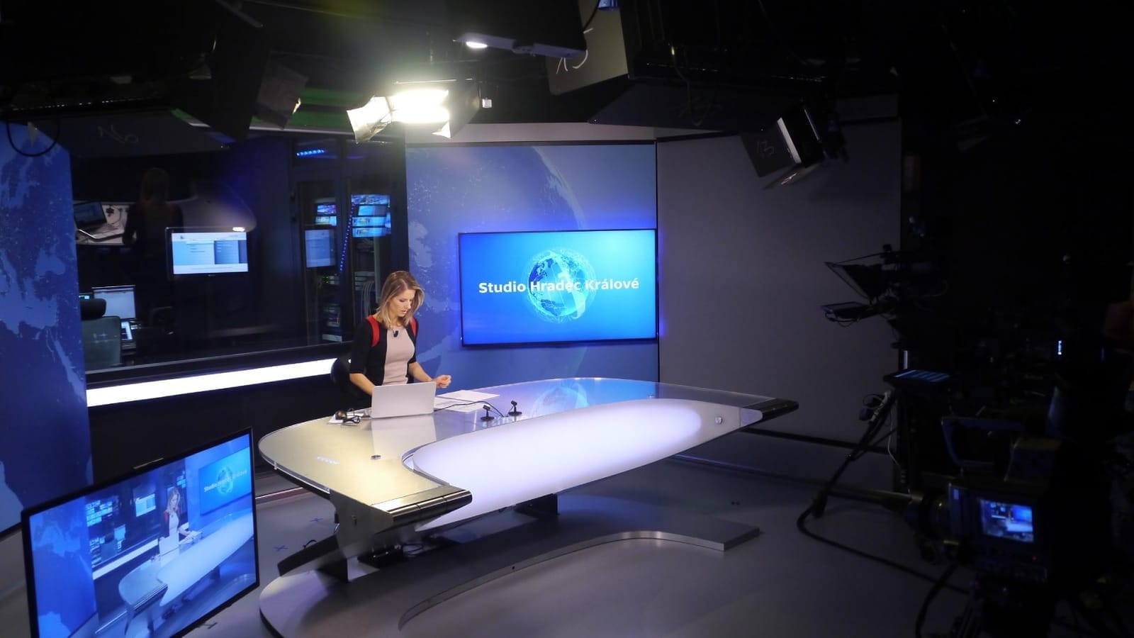 Presenter seated at a curved desk in a TV studio with a screen reading "Studio Hradec Králové"