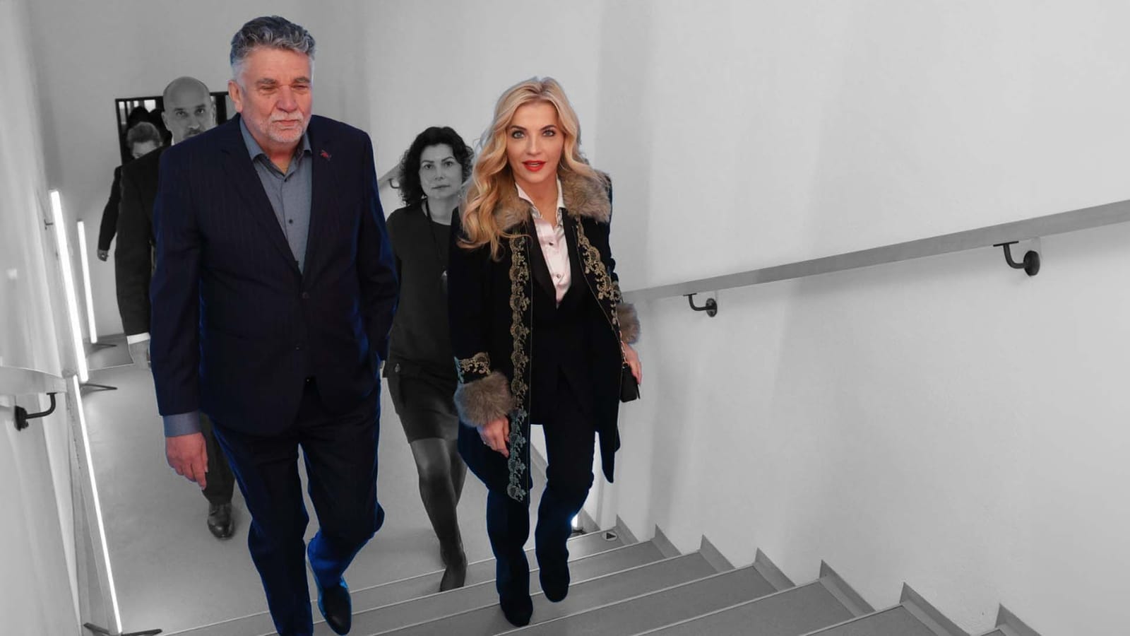 Ľuboš Machaj in a dark suit and Martina Šimkovičová in a black coat walking up a staircase, followed by two other people