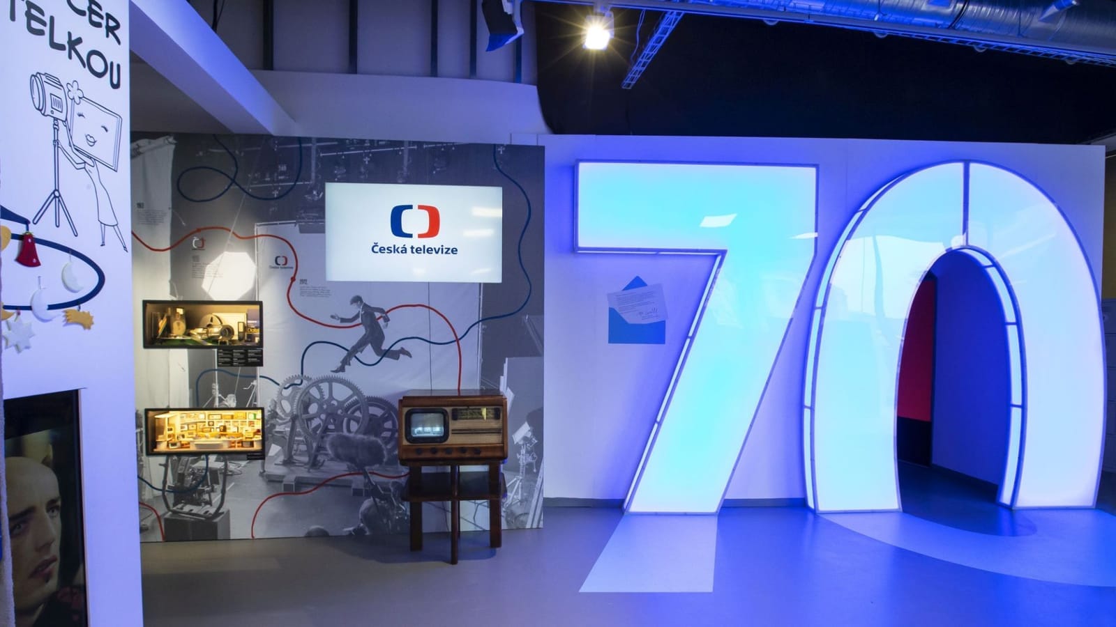 Exhibition space with a large illuminated number 70 and a Česká televize logo on a screen beside a vintage TV set