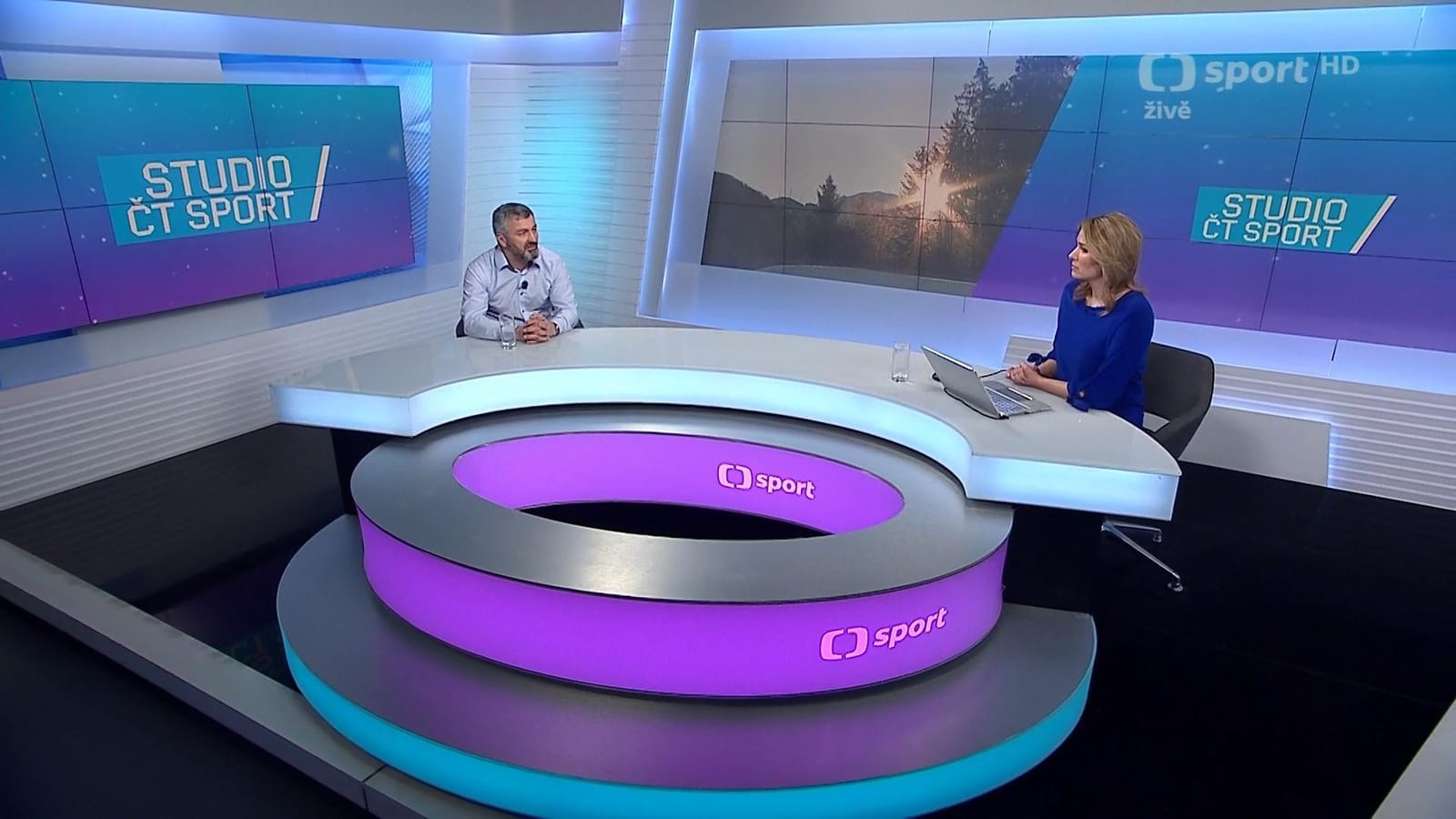 Studio ČT sport set with a female presenter at a desk interviewing a male guest, screens reading "Studio ČT sport" and "ČT sport HD, živě"