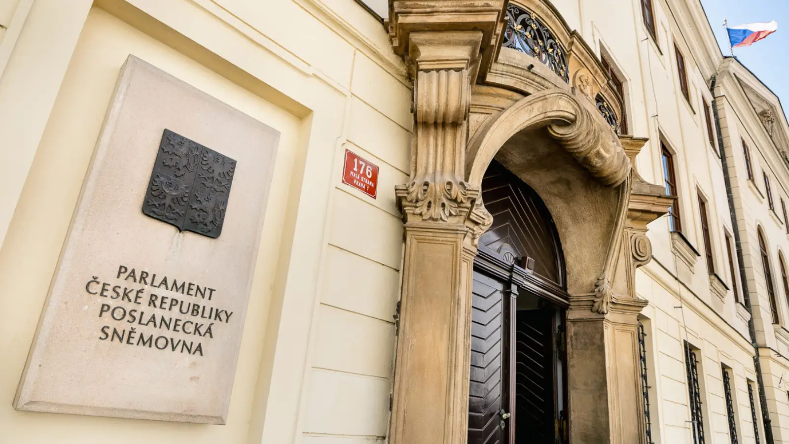 Entrance of the Czech Chamber of Deputies building with a stone plaque reading "Parlament České republiky, Poslanecká sněmovna"