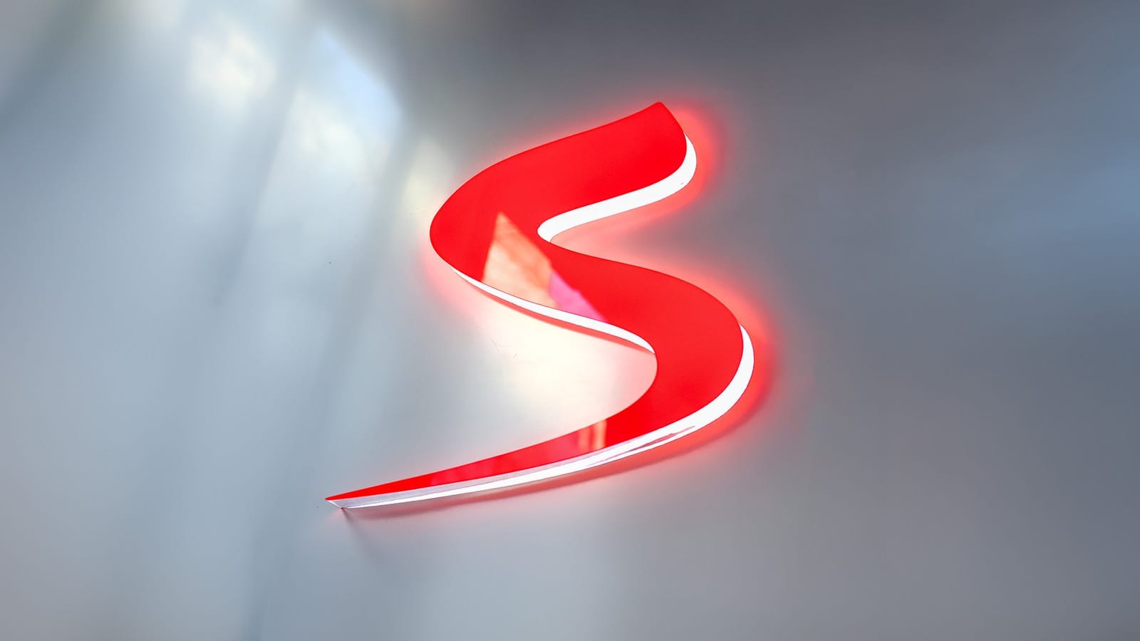 Illuminated red letter S logo of Seznam.cz mounted on a white wall