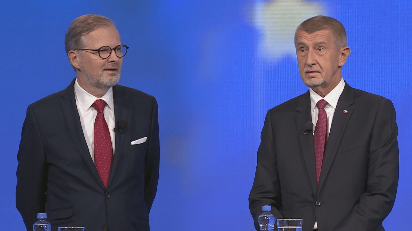 Petr Fiala and Andrej Babiš standing at lecterns in a TV debate studio against a blue backdrop