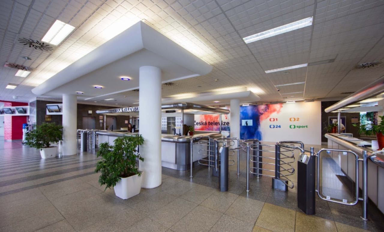 Entrance lobby of Czech Television with turnstiles and a wall sign reading "Česká televize" and channel logos ČT1, ČT2, ČT24 and ČT sport