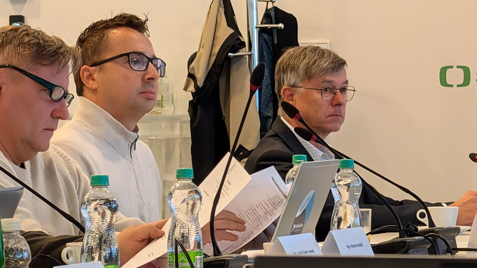 Three men at a Czech Television Council session, seated at a table with microphones, water bottles and name plates