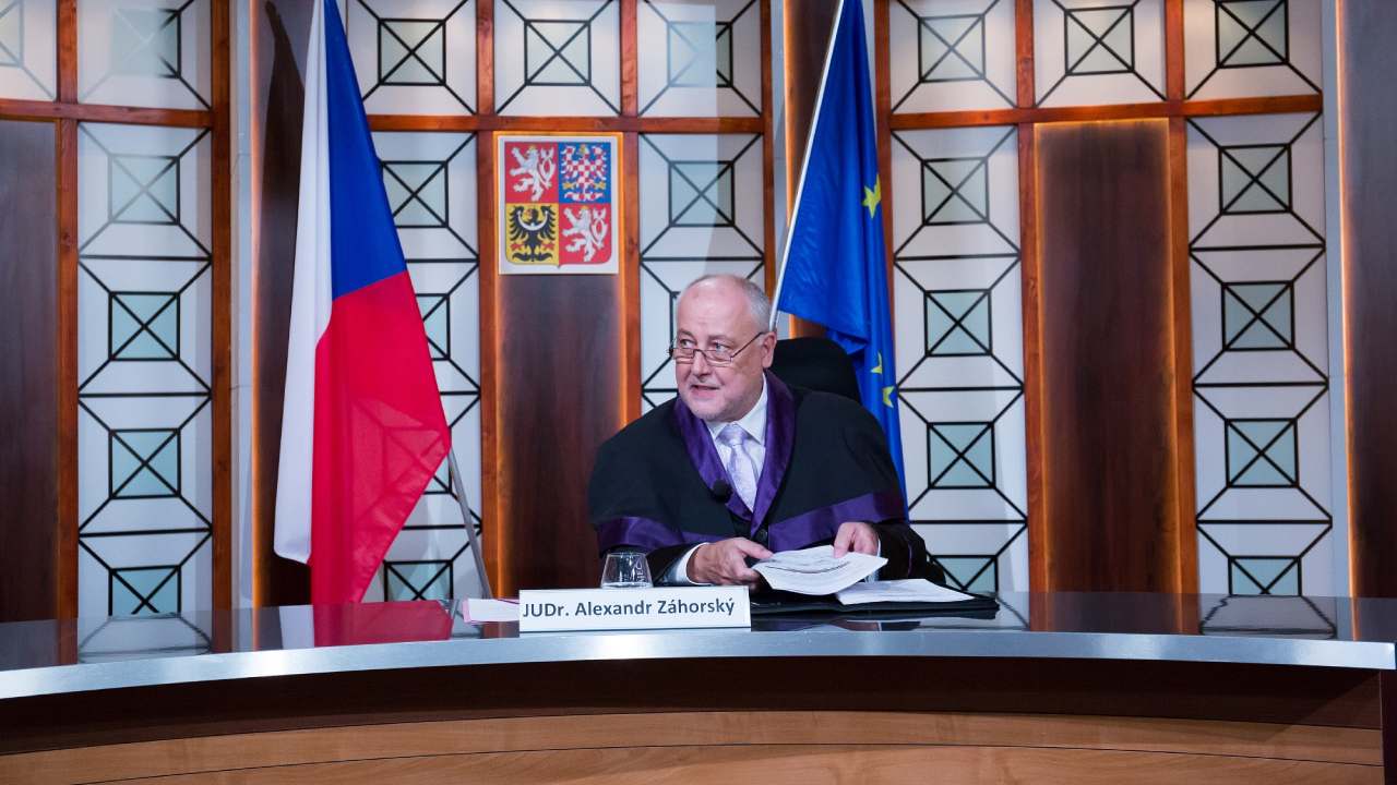 Judge JUDr. Alexandr Záhorský at his bench with Czech and EU flags and the state emblem in a TV Barrandov courtroom reality show