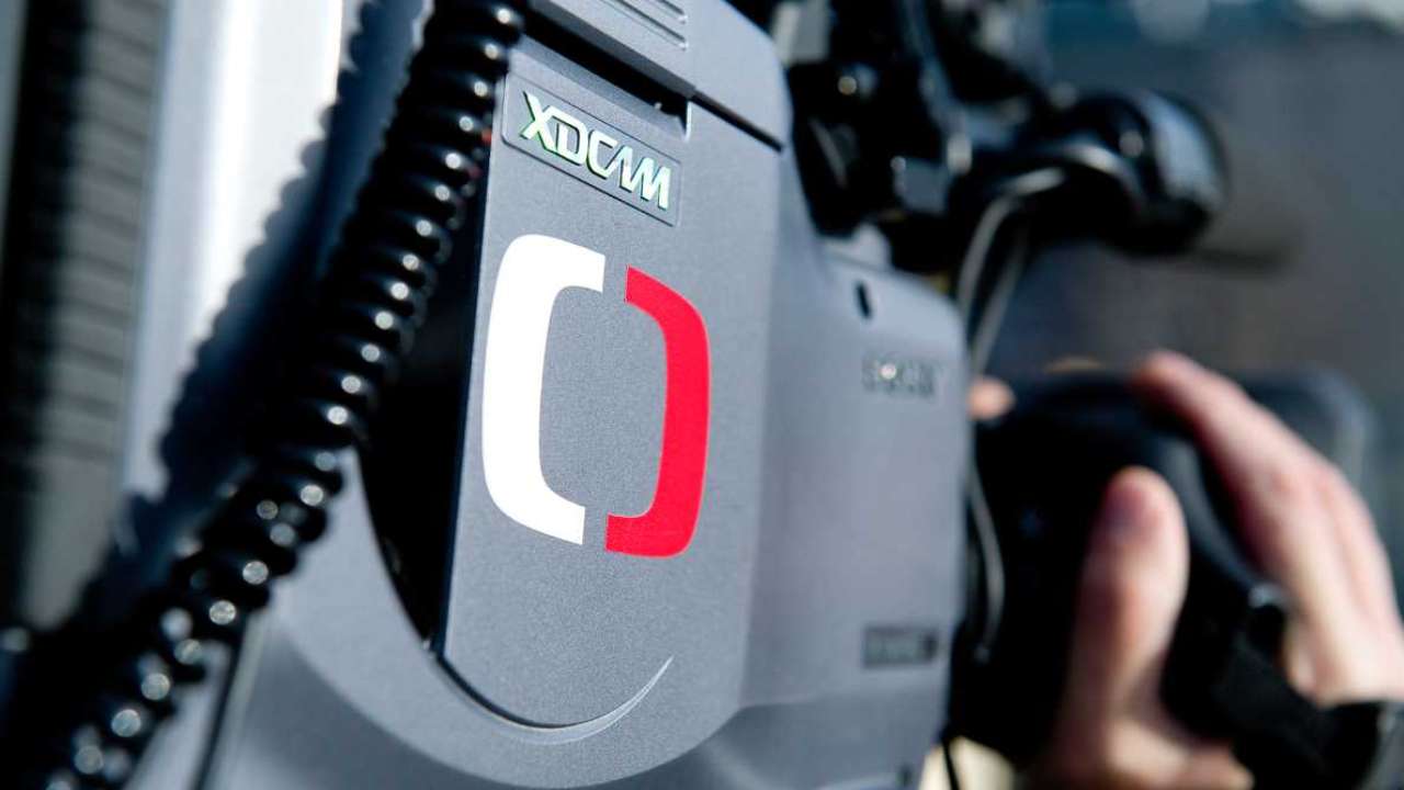 Close-up of a Sony XDCAM camera with the red and white Czech Television logo, held by a cameraman
