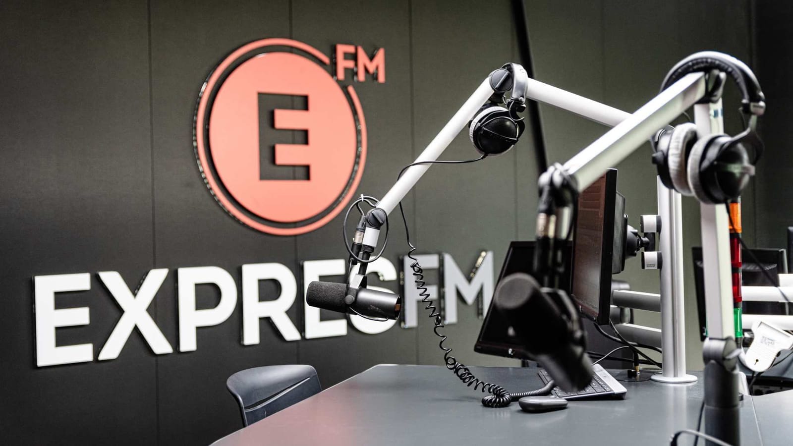 Empty radio studio with microphones, headphones and monitors in front of a wall bearing the Expres FM logo