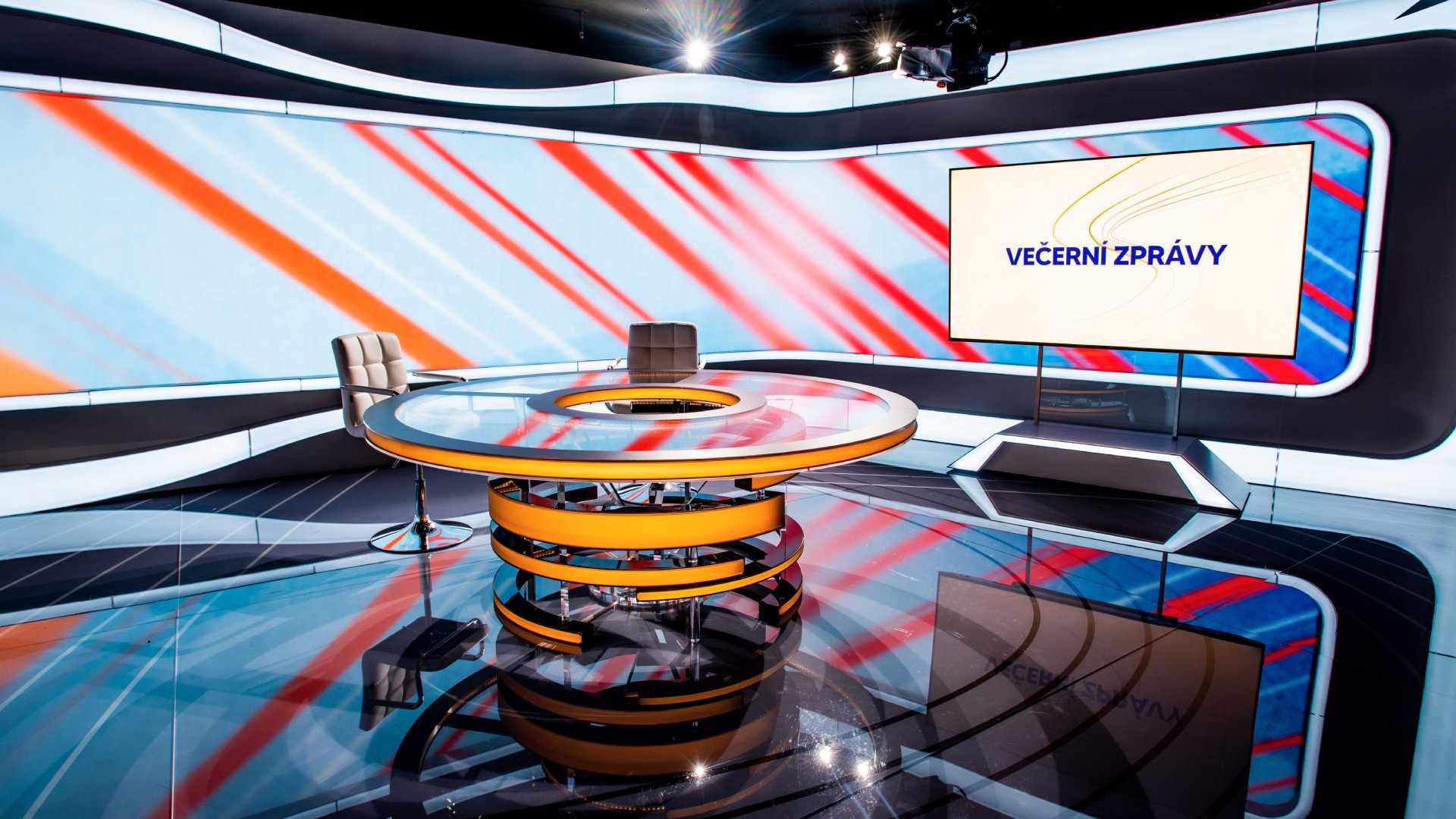 Empty TV news studio with a round orange desk and a screen reading "Večerní zprávy"