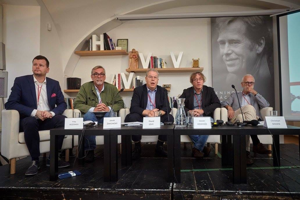 Five men on a panel behind a table with name cards reading Filip Rožánek, Jacek Žakowski, David Levy, István Hegedűs and Christian Nissen, with a portrait of Václav Havel behind them