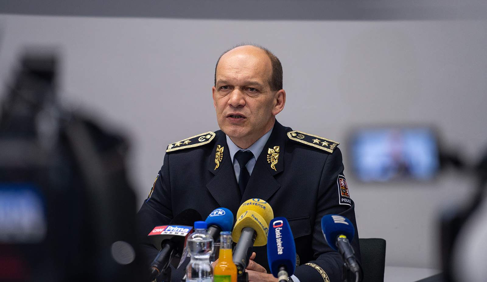 Police President Martin Vondrášek in dress uniform speaking at a press conference behind Prima and Česká televize microphones