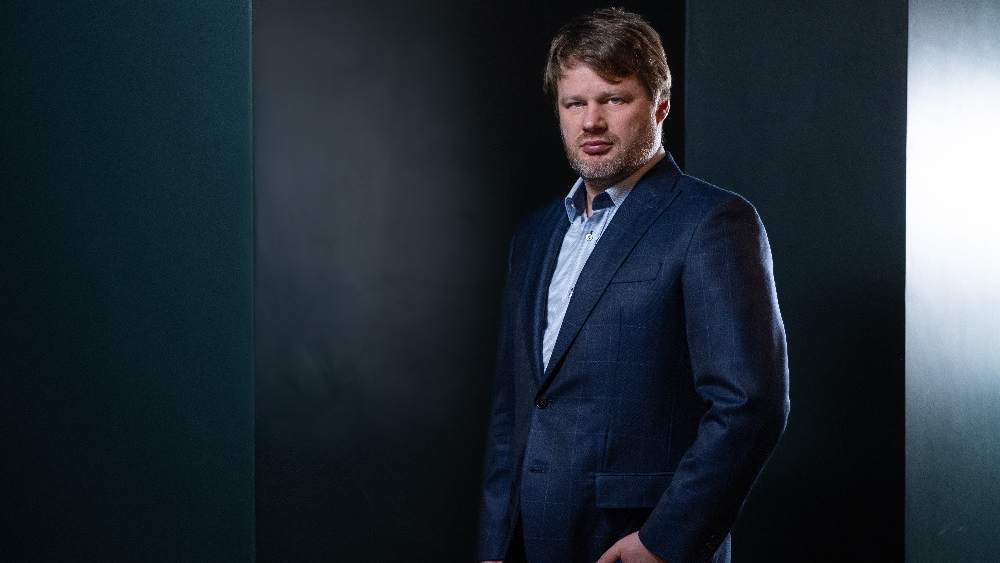 Aleš Zavoral of A11, a bearded man in a dark blue suit and light shirt, against a dark background