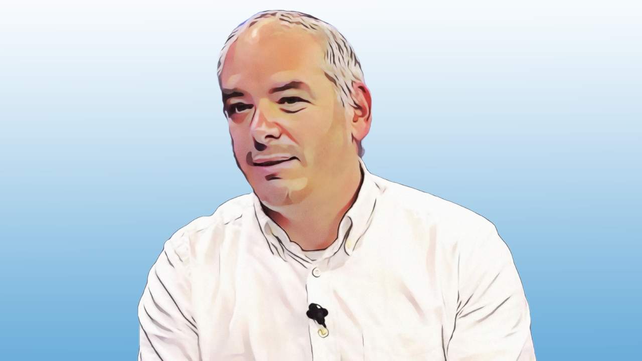Daniel Köppl in a white shirt with a clip-on microphone against a light blue background