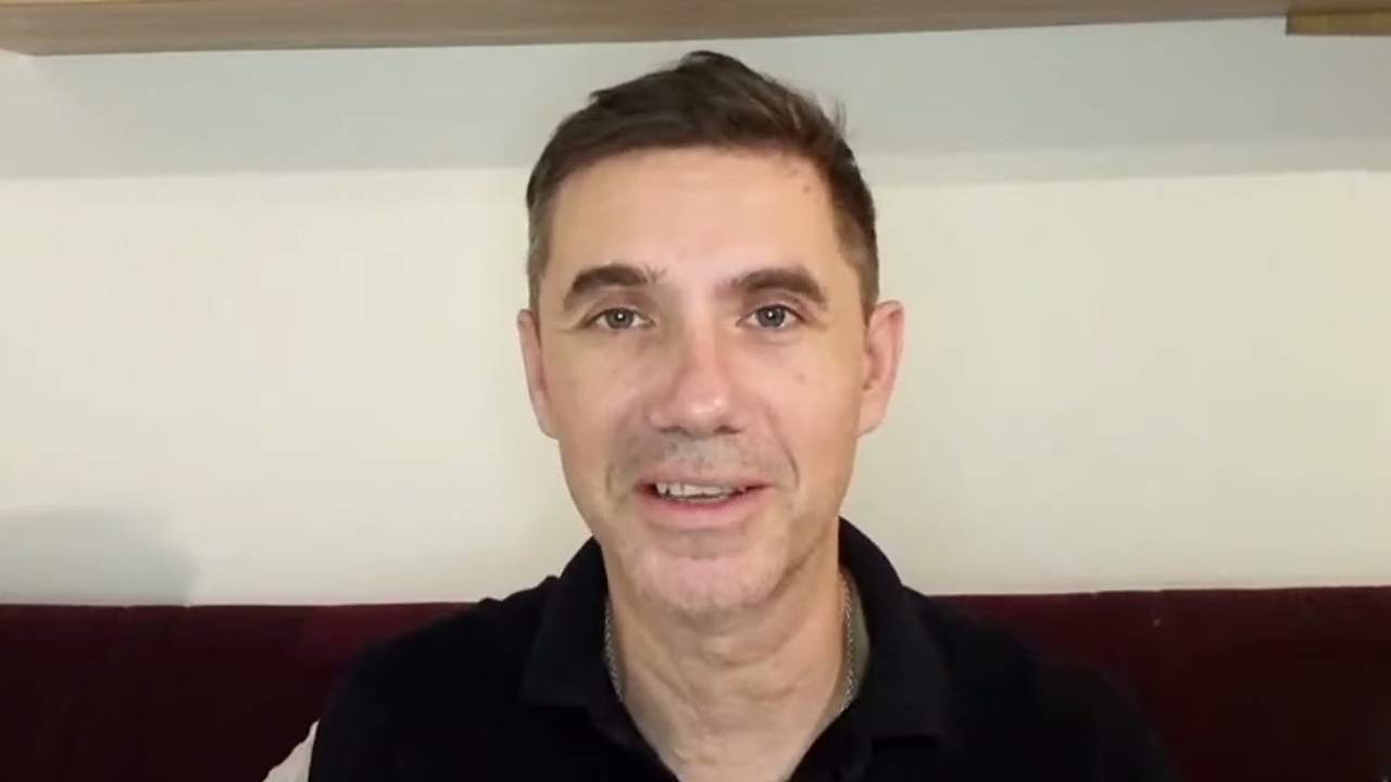 Ladislav Vrabel in a black polo shirt speaking to a webcam in front of a red sofa