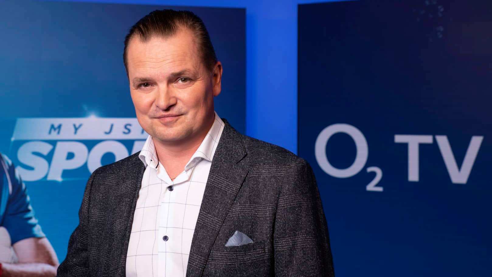 Man in a grey tweed jacket and white shirt in front of a blue backdrop with the O2 TV logo and a "MY JSME SPORT" poster