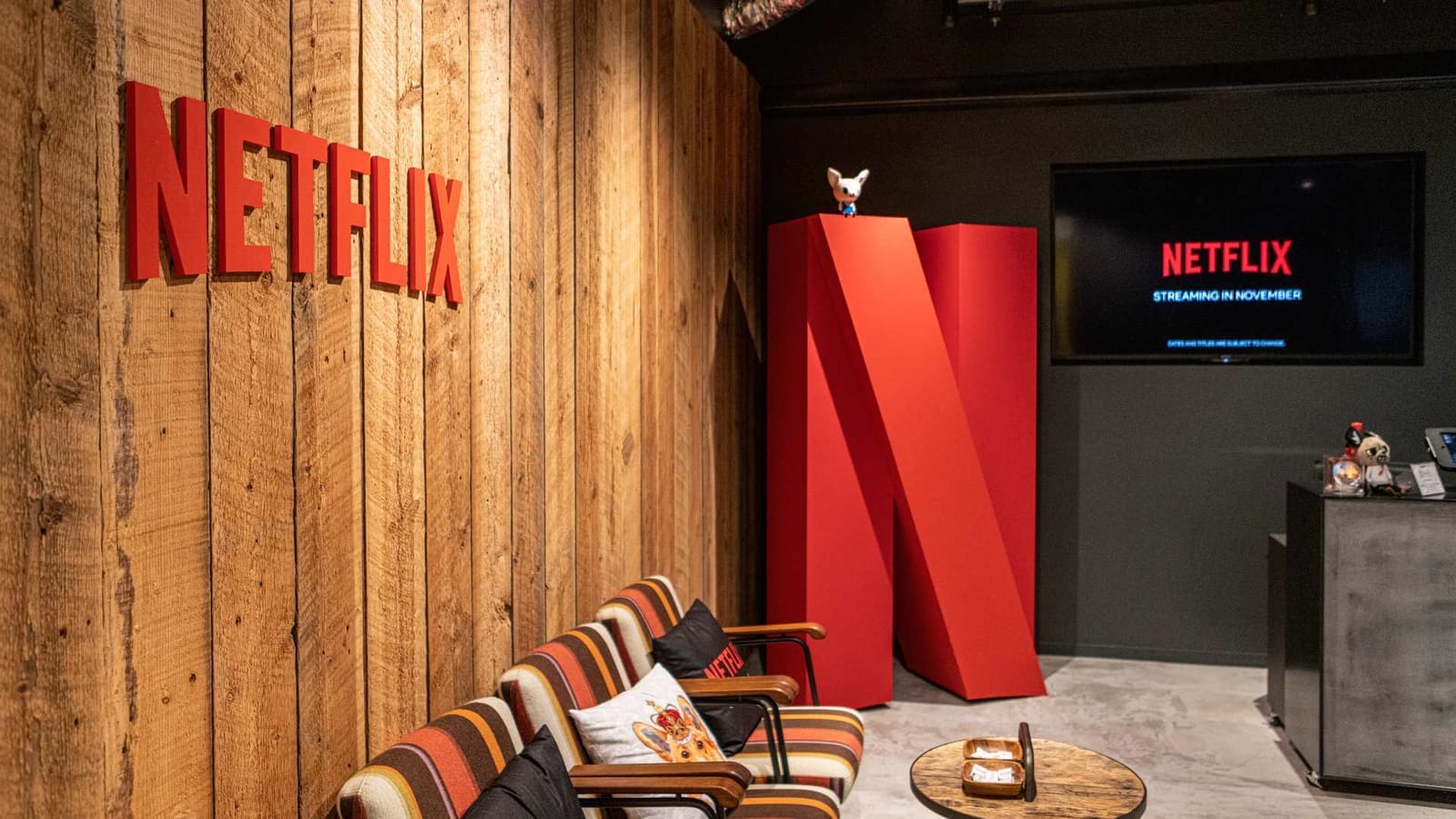Office lounge with red Netflix lettering on a wooden wall, a large red N sculpture and a screen reading "Netflix streaming in November"